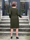 Miik founder Donna (5’6”, small) standing with her back towards the camera showing the back of Miik's Soraya long sleeve scoop neck pocket dress in olive #color_olive