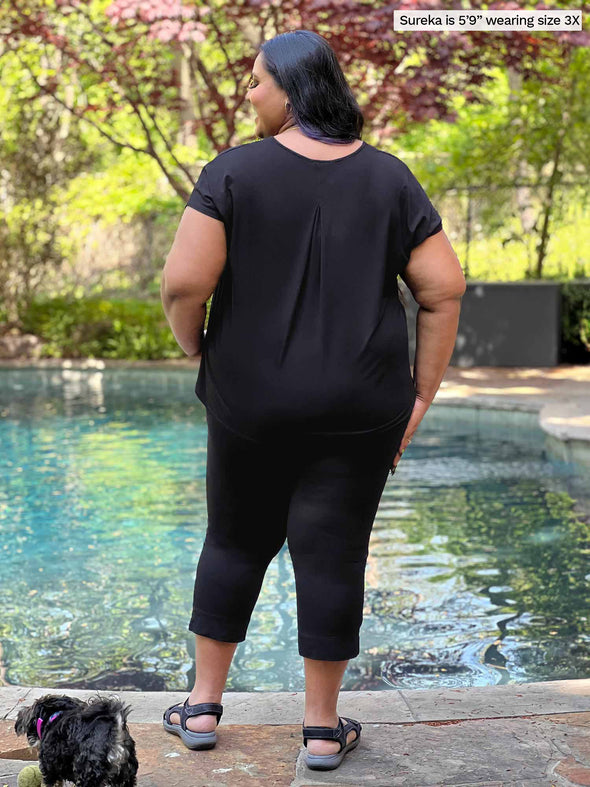 Miik model plus size Sureka (5'9", 3x) standing with her back towards the camera showing the back of Miik's Stef v-neck open-back capri jumpsuit #color_black