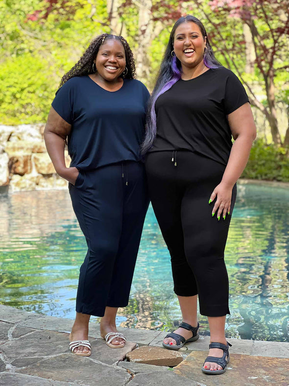 Miik models plus size Kimesha and Sureka smiling both wearing the same jumpsuit: Miik's Stef v-neck open-back capri. Kimesha is wearing in navy while Sureka is wearing in black