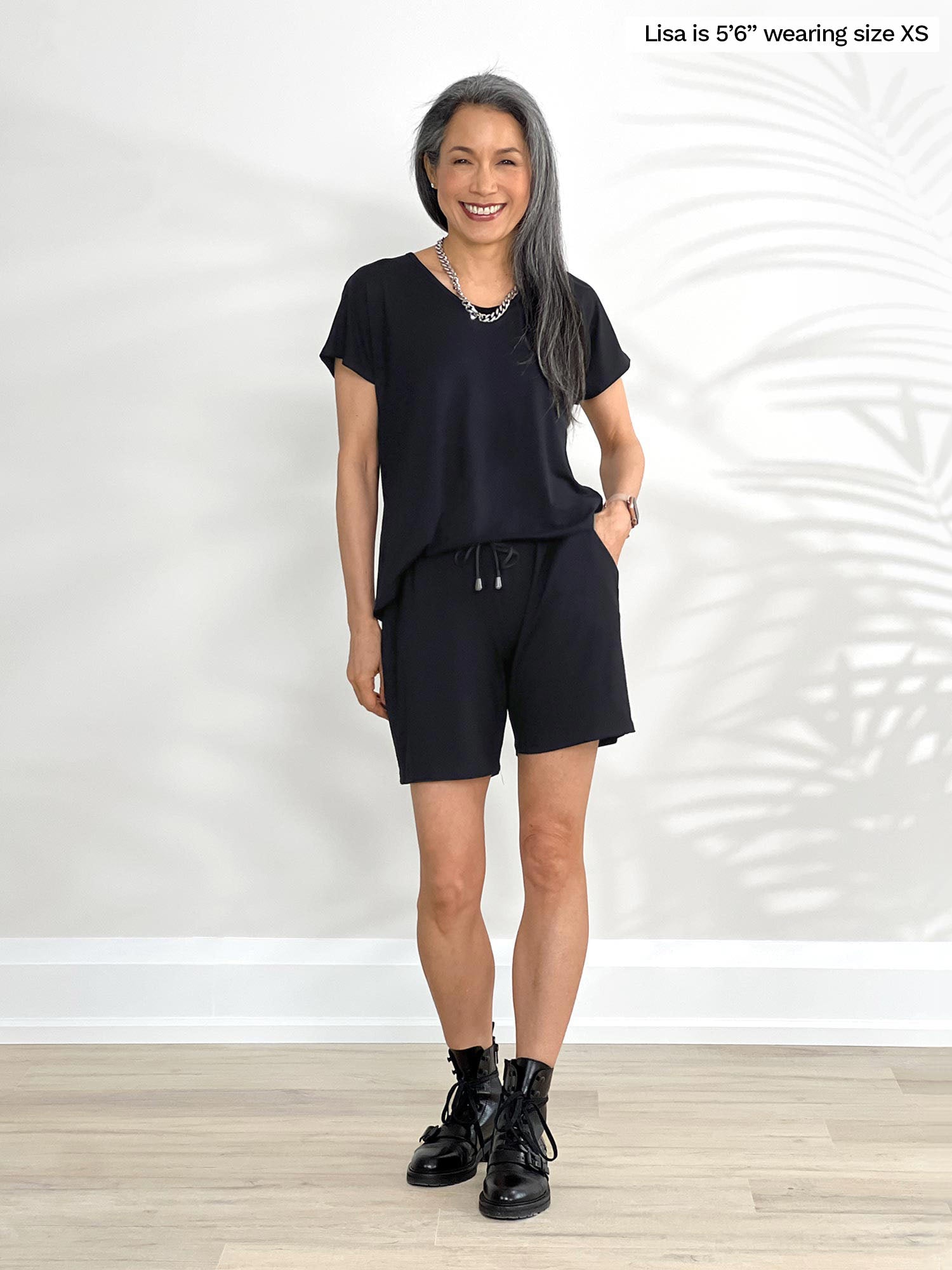 Miik model Lisa (5&quot;6, xsmall) smiling while standing in front of a white wall wearing Miik&