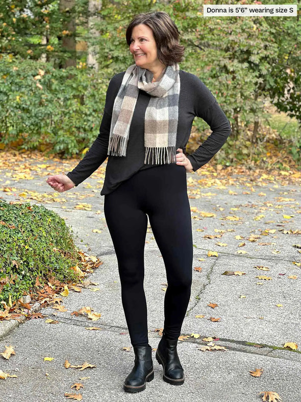 Miik founder Donna (5'6", small) smiling and looking away wearing Miik's Tinsley mid-rise fleece legging in black with a charcoal sweater, black boots and a scarf in neutral tones #color_black 