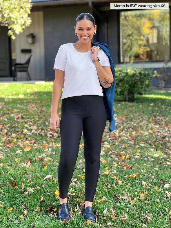 Miik model Meron (5'3", xsmall) smiling wearing Miik's Tinsley mid-rise fleece legging in black with a white tee and a blazer over shoulders #color_black