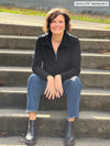 Miik founder Donna (5'6", small) sitting on a stairs wearing Miik's Tristan 1/4 zip fleece pullover in black with jeans and black boots #color_black