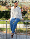 Miik model Meron (5'3", xsmall) sitting on a wall wearing Miik's Tristan 1/4 zip fleece pullover in oatmeal melange with jeans #color_oatmeal-melange 