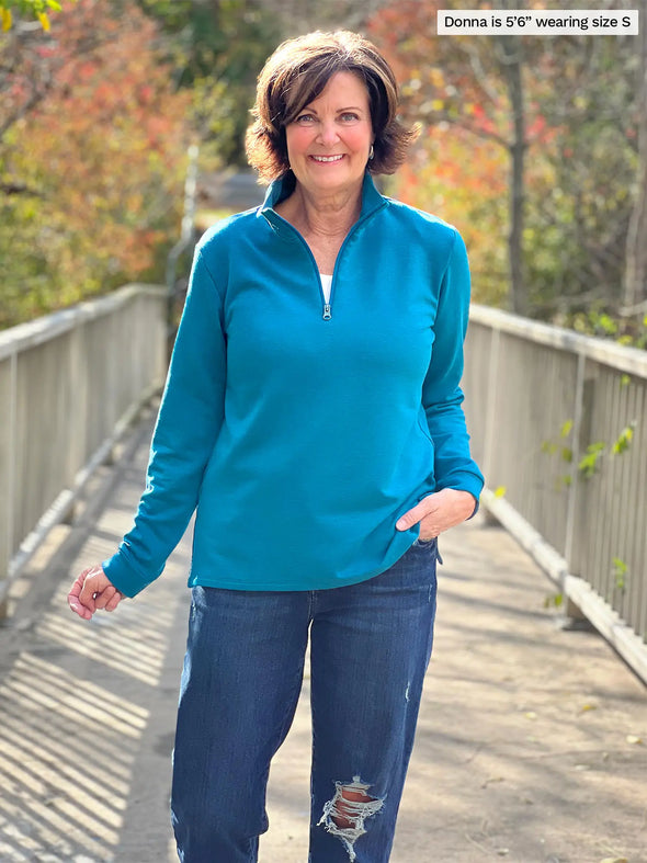 Miik founder Donna (5'6", small) smiling wearing Miik's Tristan 1/4 zip fleece pullover in teal melange with a ripped jeans #color_teal-melange 