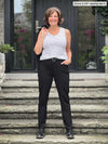 Miik founder Donna (5'6", small) smiling wearing Miik's Uma mid-rise straight leg ponte pant with pockets in black, with a belt in the same colour and a striped tank top #color_black