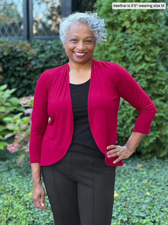 Miik model Keethai (5'5", medium) smiling wearing Miik's Wesley cropped cardigan in cerise and an all black ourtit: v-neck tee and dress pant 
#color_cerise 