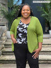 Miik model plus size Kimesha (5'8", 3x) smiling wearing Miik's Wesley cropped cardigan in green moss with a printed floral tank and a black pant  