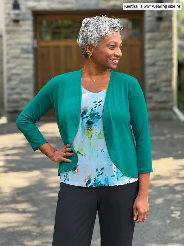 Miik model Keethai (5'5", medium) smiling and looking away wearing Miik's Wesley cropped cardigan in jade melange along with a printed tank top and a charcoal pant 
#color_jade-melange 