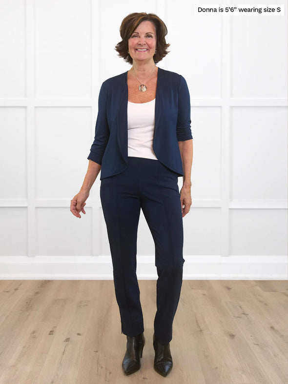 Miik founder Donna (5'6", small) smiling white standing in front of a white wall wearing Miik's Wesley cropped cardigan in navy with a dress pant in the same colour and a white tank top 
#color_navy