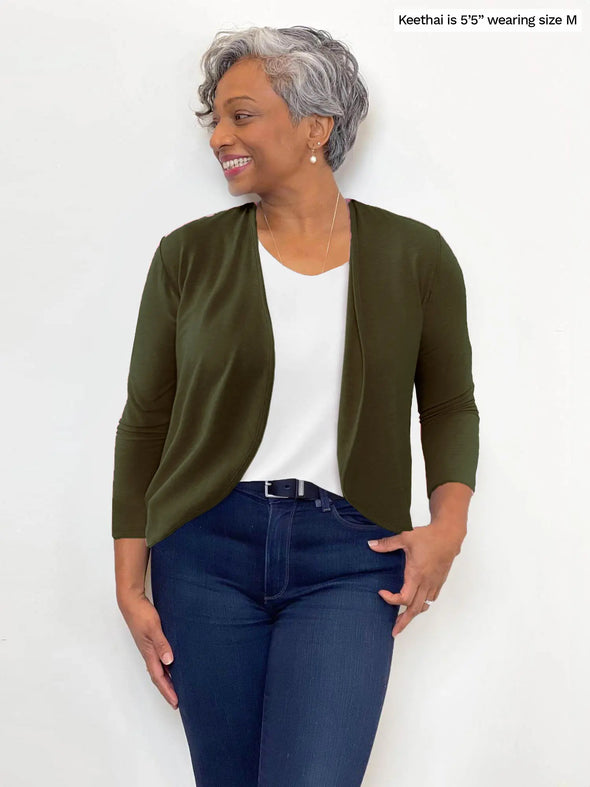 Miik model Keethai (5'5", medium) smiling and looking away wearing Miik's Wesley cropped cardigan in olive gree with a tank top in white and jeans 
#color_olive 