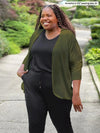 Miik model Kimesha (5'8", 3x, plus size) smiling and looking away wearing Miik's Wesley cropped cardigan in olive with a black jumpsuit 
#color_olive 