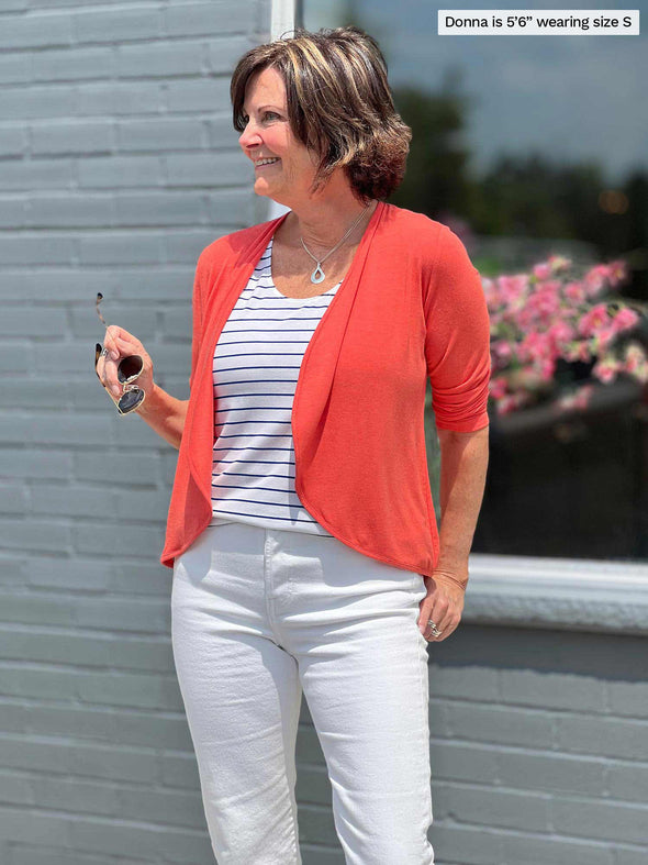 Miik founder Donna (5'6", small) looking away while wearing Miik's Wesley cropped cardigan in papaya, a white striped tank and white jeans
