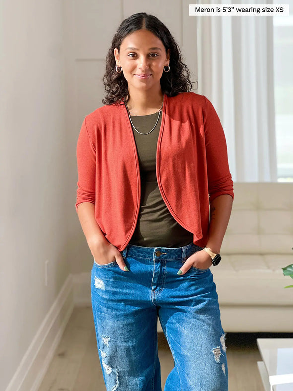 Miik model Meron (5'3", xsmall) smiling wearing Miik's Wesley cropped cardigan in paprika melange along with a olive tank top and jeans 
#color_paprika-melange 