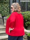 Miik model plus size Kelly (5’7”, 3x) standing with her back towards the camera showing the back of Miik's Wesley cropped cardigan in poppy red 