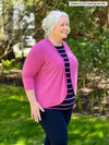 Miik model Colleen (5'3", xxlarge) smiling while standing sideway wearing Miik's Wesley cropped cardigan in pretty in pink, striped tank and a navy legging 