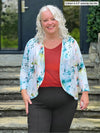 Miik model Colleen (5'3", xxlarge) smiling wearing a paprika melange tank, charcoal dress pant and Miik's Wesley cropped cardigan in water lily print 
#color_water-lily