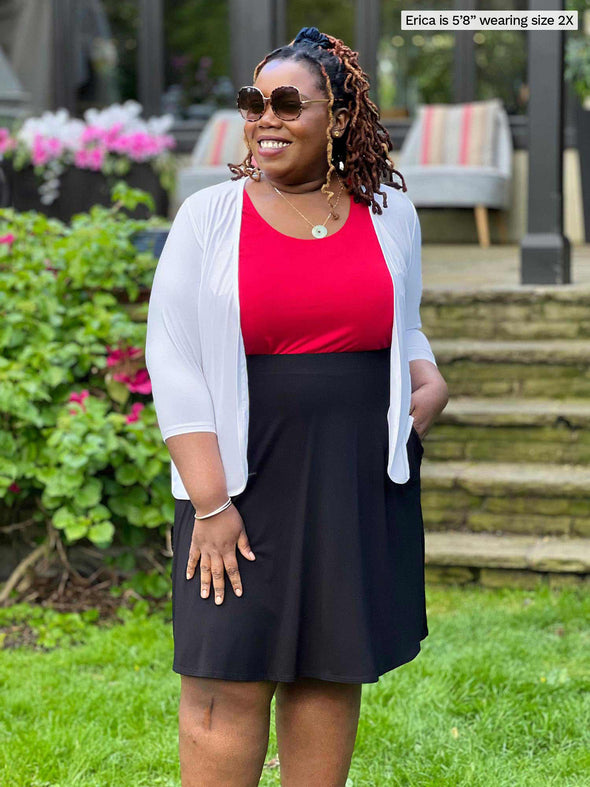 Miik model plus size Erica (5'8", 2x) smiling and looking away wearing Miik's Wesley cropped cardigan in white with a poppy red tank and a flouncy skirt in black 