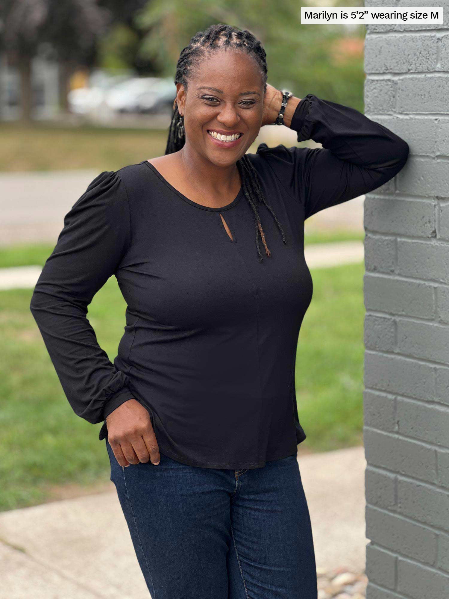 Woman smiling while leaning against a brick wall wearing Miik&