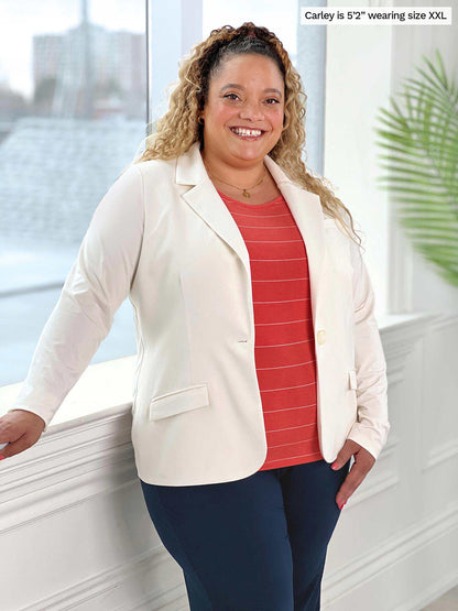 Miik model Carley (five feet two, size double extra large) smiling in front of a window wearing a striped top in papaya, navy pant and Miik&